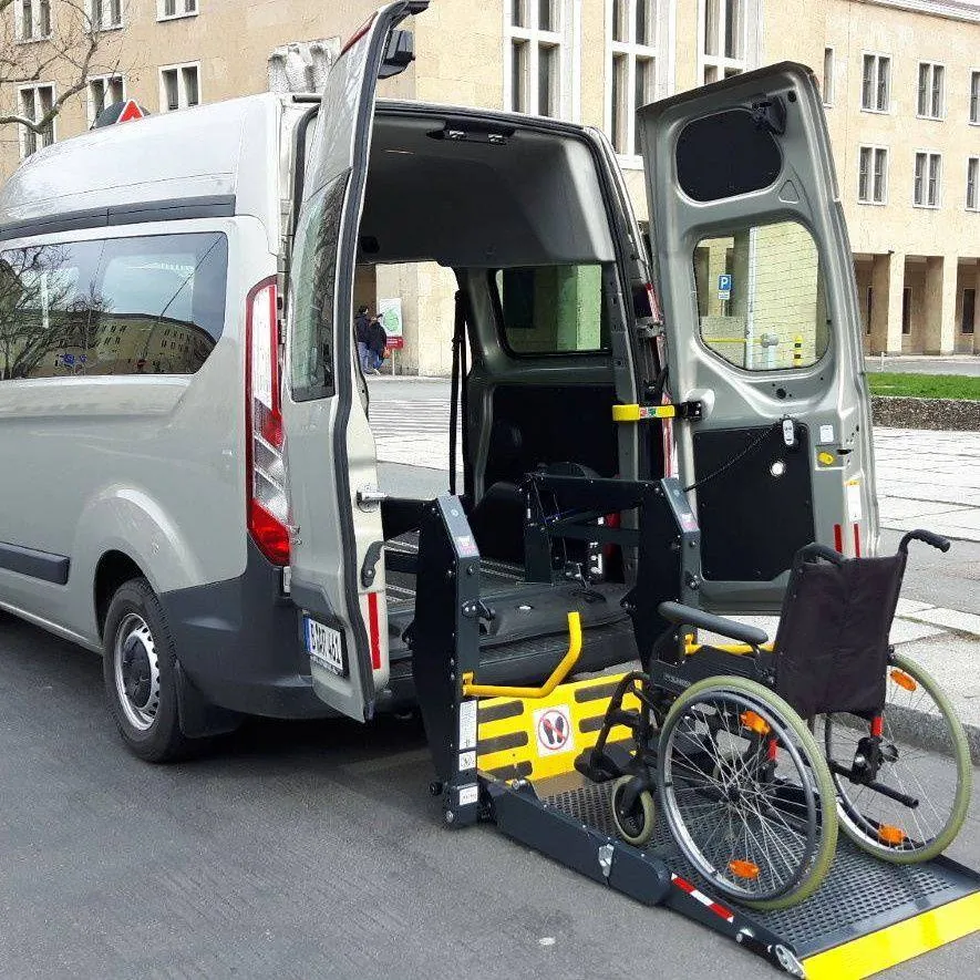 Mikrobusz nyitott hátsó ajtókkal, lehajtott kerekesszékes lifttel és kerekesszékkel a platformon